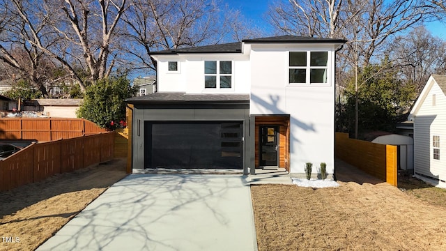 contemporary home with a shingled roof, concrete driveway, an attached garage, fence, and stucco siding