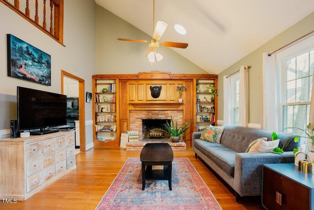 living room featuring light wood-style floors, a fireplace, high vaulted ceiling, and a ceiling fan