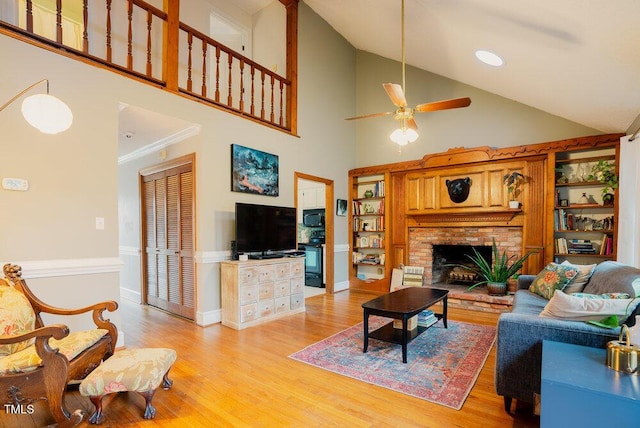 living area with a brick fireplace, baseboards, ceiling fan, light wood-style floors, and high vaulted ceiling