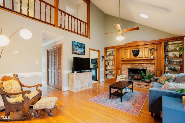 living area featuring light wood-style floors, a ceiling fan, a brick fireplace, high vaulted ceiling, and baseboards