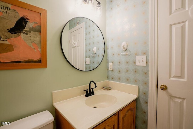 bathroom with vanity, toilet, and wallpapered walls