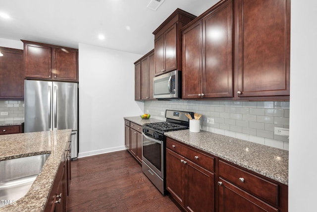 kitchen with light stone counters, stainless steel appliances, visible vents, backsplash, and dark wood-style floors