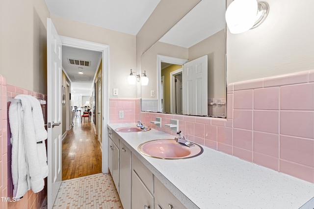 bathroom with a wainscoted wall, tile walls, double vanity, visible vents, and a sink