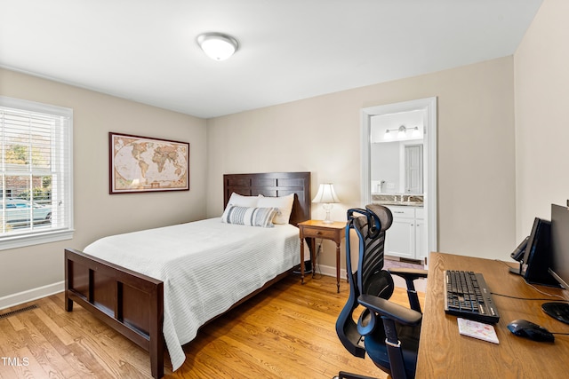 bedroom with light wood-style floors, visible vents, baseboards, and ensuite bathroom