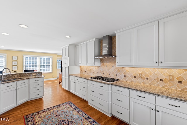 kitchen featuring light wood-style floors, light stone countertops, wall chimney range hood, white cabinetry, and a sink