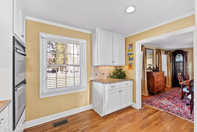 kitchen with stone counters, white cabinets, crown molding, and visible vents