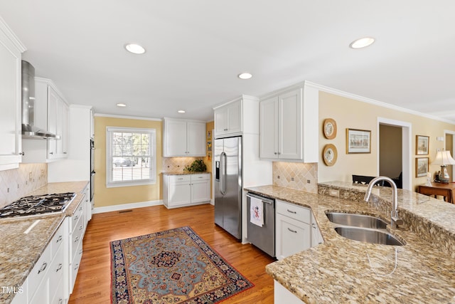 kitchen with wall chimney range hood, appliances with stainless steel finishes, white cabinets, and a sink