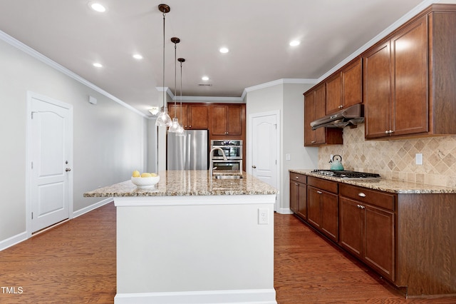 kitchen with appliances with stainless steel finishes, a center island with sink, hanging light fixtures, dark wood-type flooring, and light stone countertops