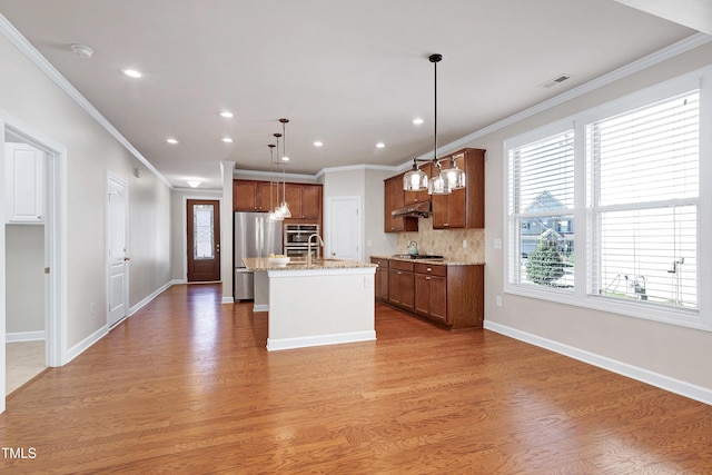 kitchen with backsplash, light wood-type flooring, pendant lighting, stainless steel appliances, and an island with sink