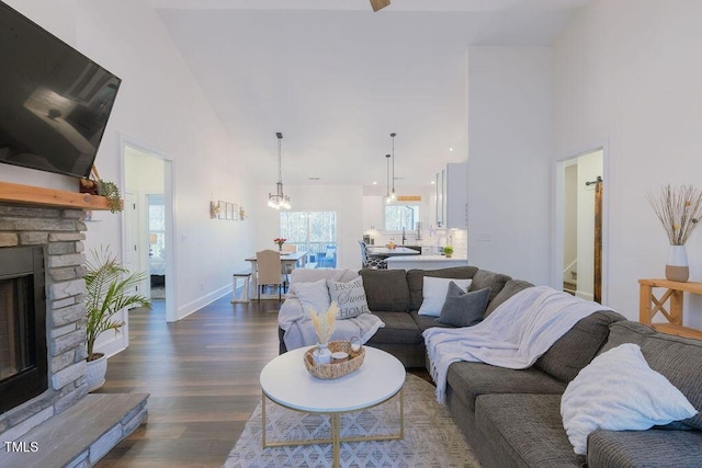 living area featuring dark wood-style floors, baseboards, a stone fireplace, and a towering ceiling