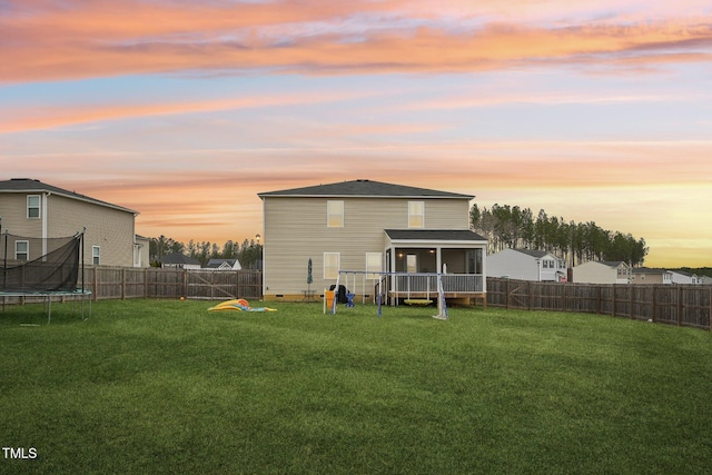 back house at dusk featuring a trampoline, a lawn, and a sunroom