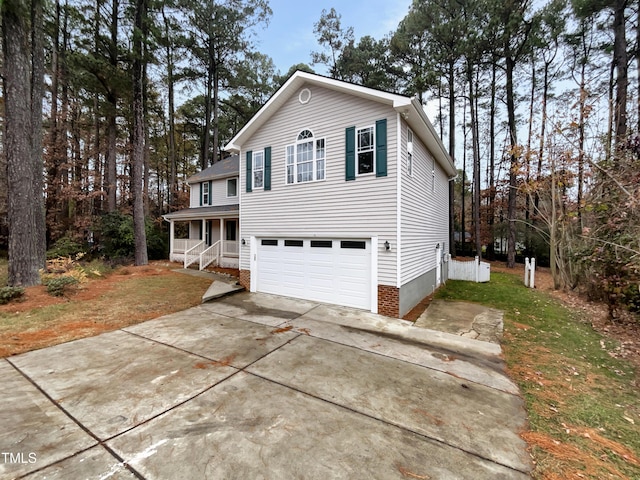 view of side of property featuring covered porch, driveway, a yard, and an attached garage