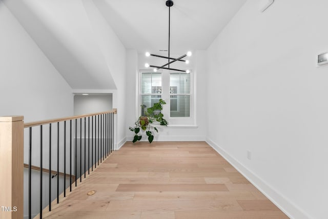 corridor featuring light wood finished floors, baseboards, and a notable chandelier