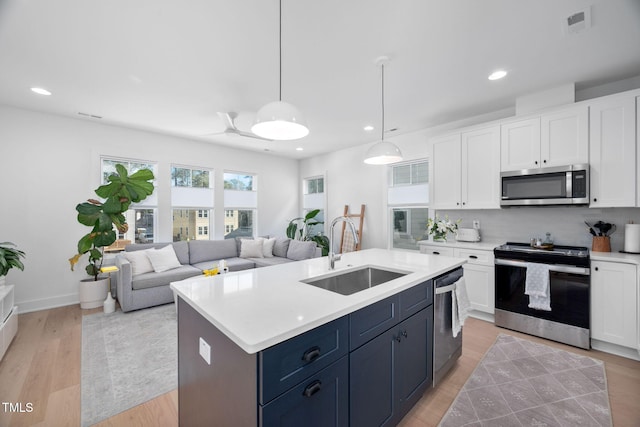 kitchen with appliances with stainless steel finishes, open floor plan, light countertops, and a sink