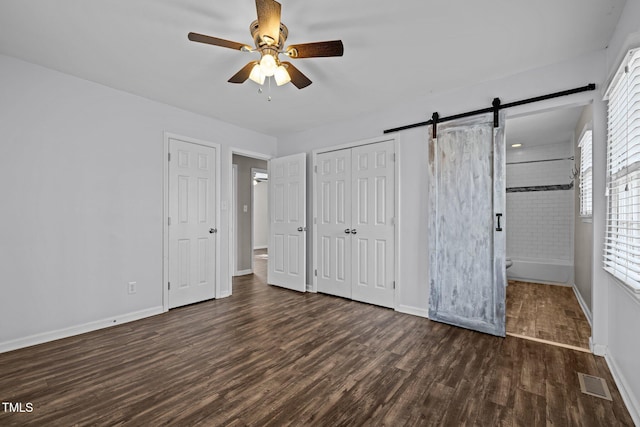 unfurnished bedroom featuring visible vents, a barn door, ensuite bath, wood finished floors, and baseboards