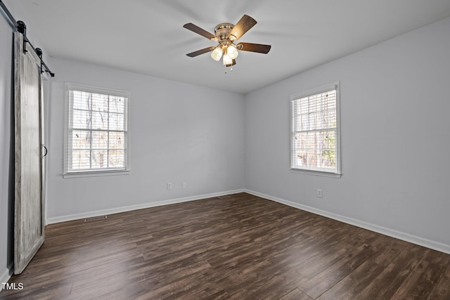 unfurnished room featuring a barn door, baseboards, visible vents, dark wood finished floors, and a ceiling fan