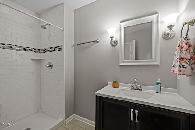 bathroom with baseboards, a tile shower, and vanity