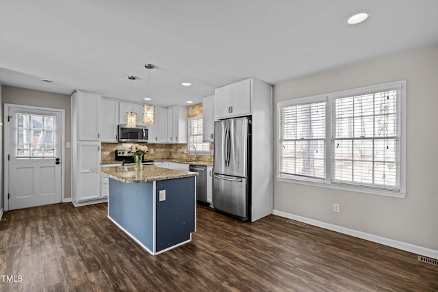 kitchen featuring stainless steel appliances, a kitchen island, a sink, white cabinets, and tasteful backsplash