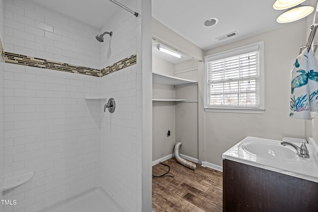 full bath featuring vanity, visible vents, tiled shower, and wood finished floors