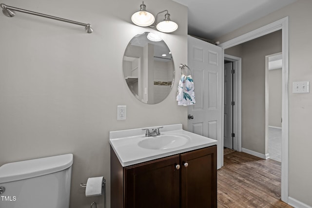 bathroom featuring toilet, baseboards, wood finished floors, and vanity