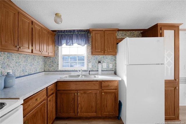 kitchen with light countertops, a sink, freestanding refrigerator, and brown cabinets