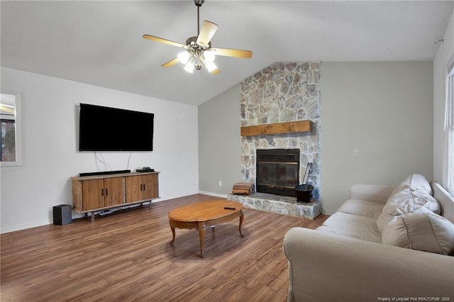 living room featuring hardwood / wood-style flooring, ceiling fan, vaulted ceiling, and a stone fireplace