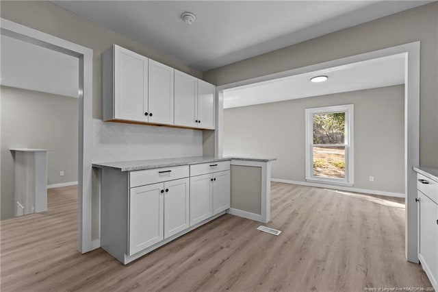 kitchen featuring light stone countertops, light wood-type flooring, white cabinetry, and tasteful backsplash