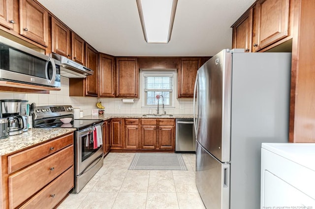 kitchen with sink, light stone counters, stainless steel appliances, washer / dryer, and decorative backsplash