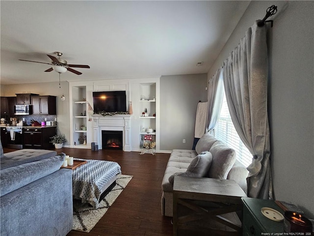 living room with dark wood-type flooring, built in shelves, and ceiling fan