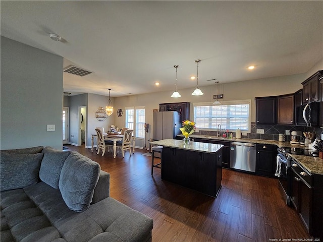 kitchen featuring a kitchen island, sink, stone counters, appliances with stainless steel finishes, and pendant lighting