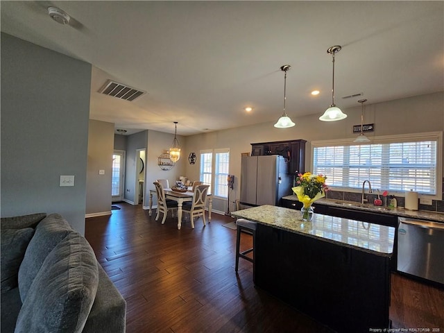 kitchen featuring hanging light fixtures, dishwasher, a kitchen island, sink, and fridge