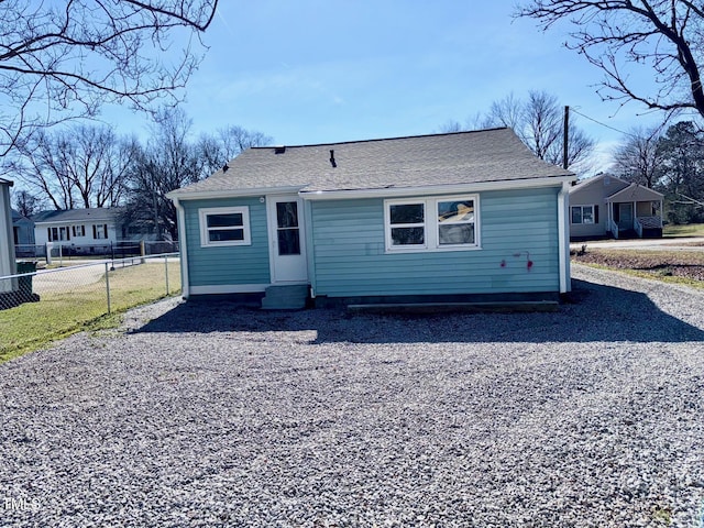 back of property with entry steps, roof with shingles, fence, and driveway