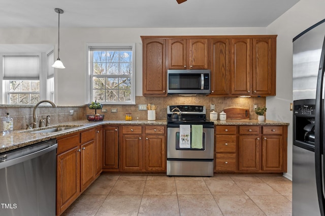 kitchen with a sink, hanging light fixtures, appliances with stainless steel finishes, tasteful backsplash, and brown cabinetry