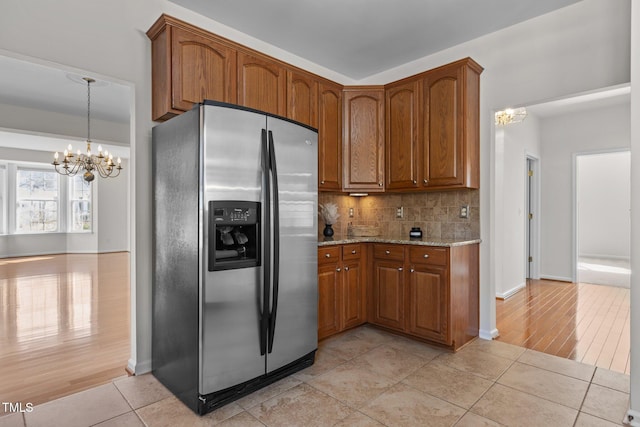 kitchen with pendant lighting, brown cabinets, stainless steel refrigerator with ice dispenser, tasteful backsplash, and a chandelier