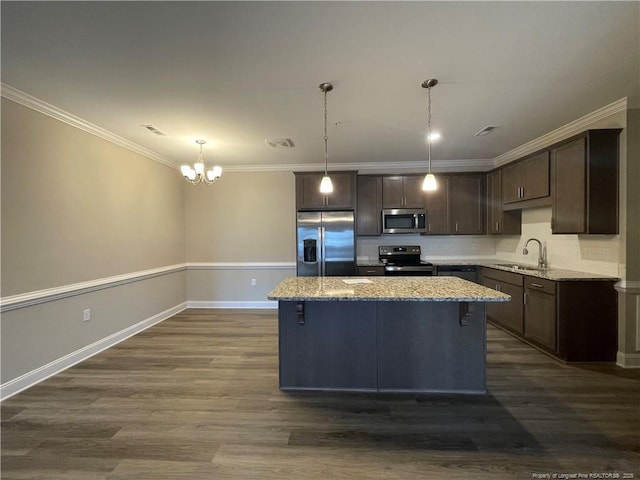 kitchen with appliances with stainless steel finishes, sink, light stone counters, a kitchen island, and hanging light fixtures