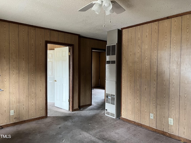 unfurnished bedroom with a ceiling fan, a heating unit, carpet flooring, wood walls, and a textured ceiling