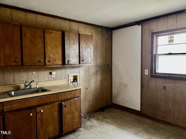 kitchen with light floors, a sink, wooden walls, a textured ceiling, and baseboards