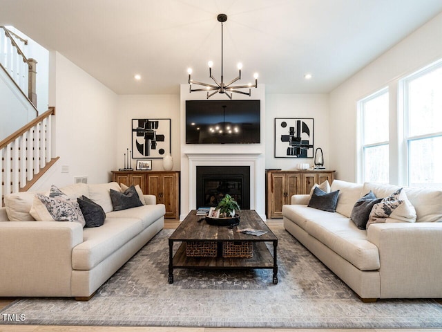 living area featuring stairway, recessed lighting, a glass covered fireplace, and a notable chandelier