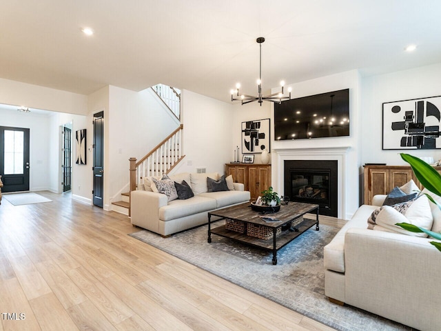 living area with an inviting chandelier, light wood-style floors, a glass covered fireplace, baseboards, and stairs