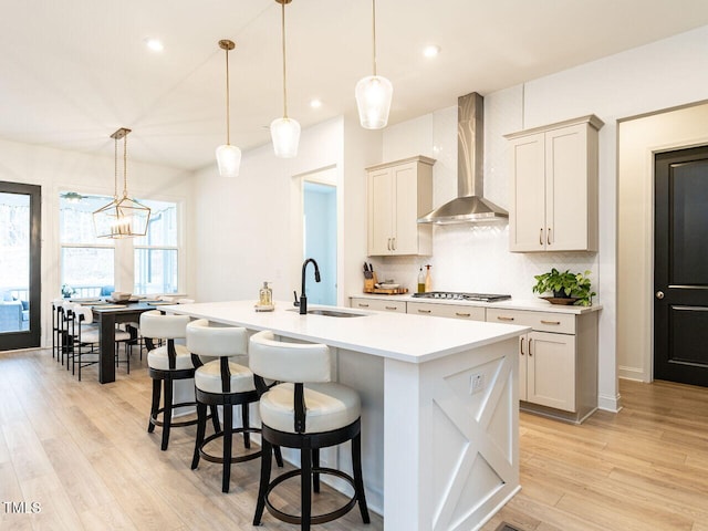 kitchen featuring hanging light fixtures, wall chimney range hood, light countertops, and a sink