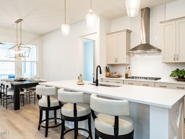 kitchen featuring pendant lighting, stainless steel gas cooktop, light countertops, a sink, and wall chimney range hood