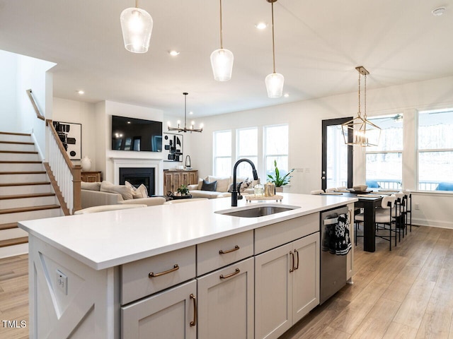 kitchen with an island with sink, pendant lighting, light countertops, and a sink