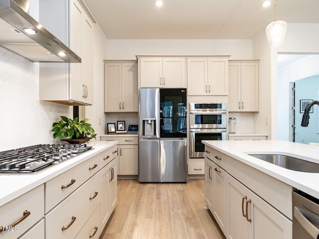 kitchen featuring stainless steel appliances, range hood, light countertops, and hanging light fixtures