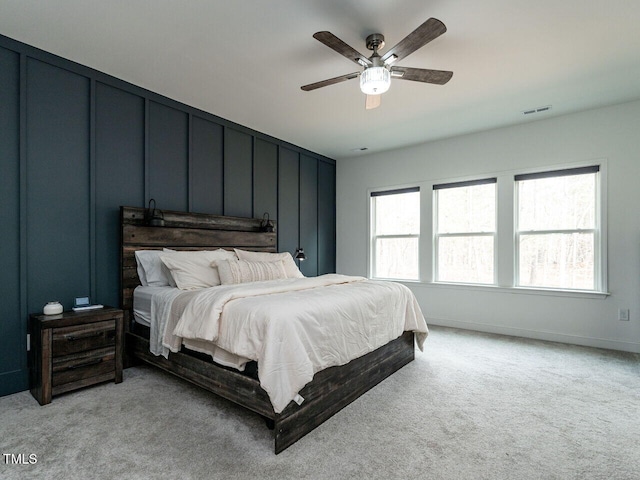 bedroom with ceiling fan, visible vents, a decorative wall, and light colored carpet