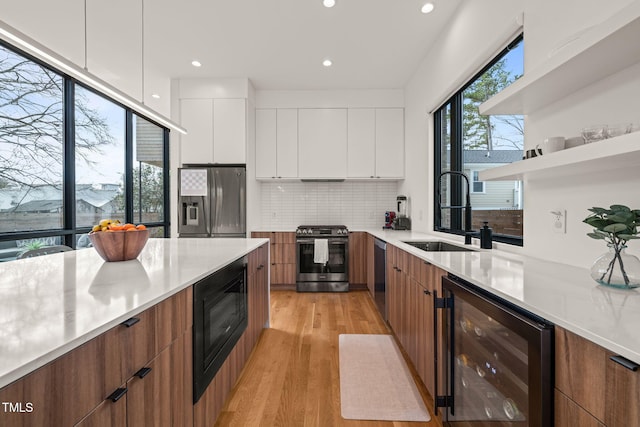 kitchen featuring wine cooler, stainless steel appliances, brown cabinetry, a sink, and modern cabinets