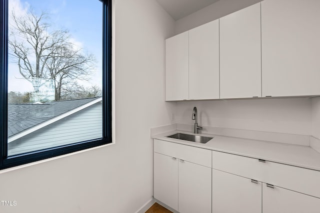 kitchen featuring baseboards, light countertops, a sink, and white cabinets