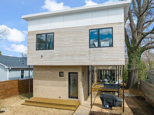 rear view of property with fence, a deck, and brick siding