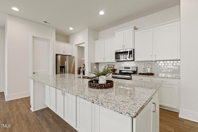 kitchen with appliances with stainless steel finishes, wood finished floors, white cabinets, and decorative backsplash