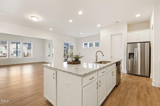 kitchen with stainless steel appliances, a sink, a kitchen island with sink, and light wood-style floors