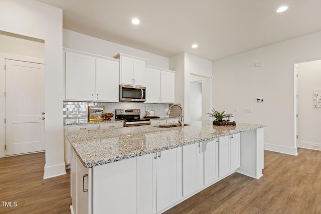 kitchen featuring wood finished floors, a sink, white cabinetry, appliances with stainless steel finishes, and backsplash